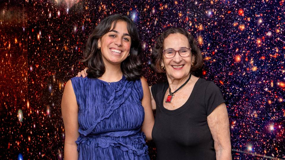 Sophia Varughese and Neta Bahcall in front of Hubble photograph of stars and galaxies