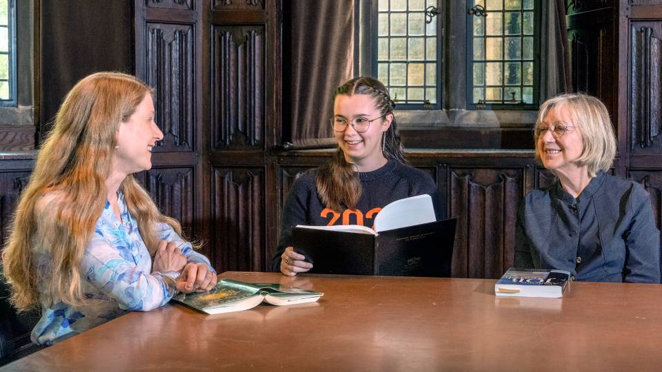 Student Nora Graves sits at a table holding her thesis with Professors Christiane Fellbaum and Laura Kalin on her left and right