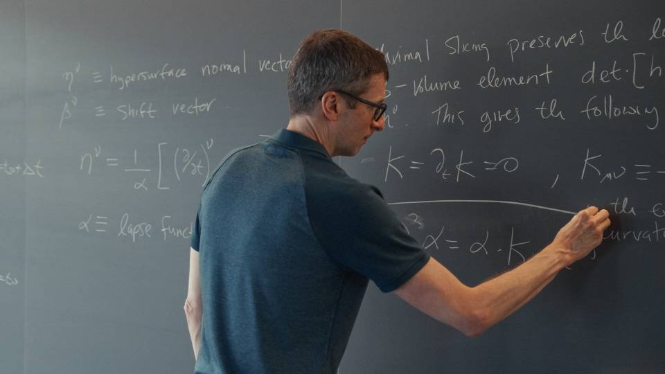 Physics professor Frans Pretorius writes equations at the blackboard