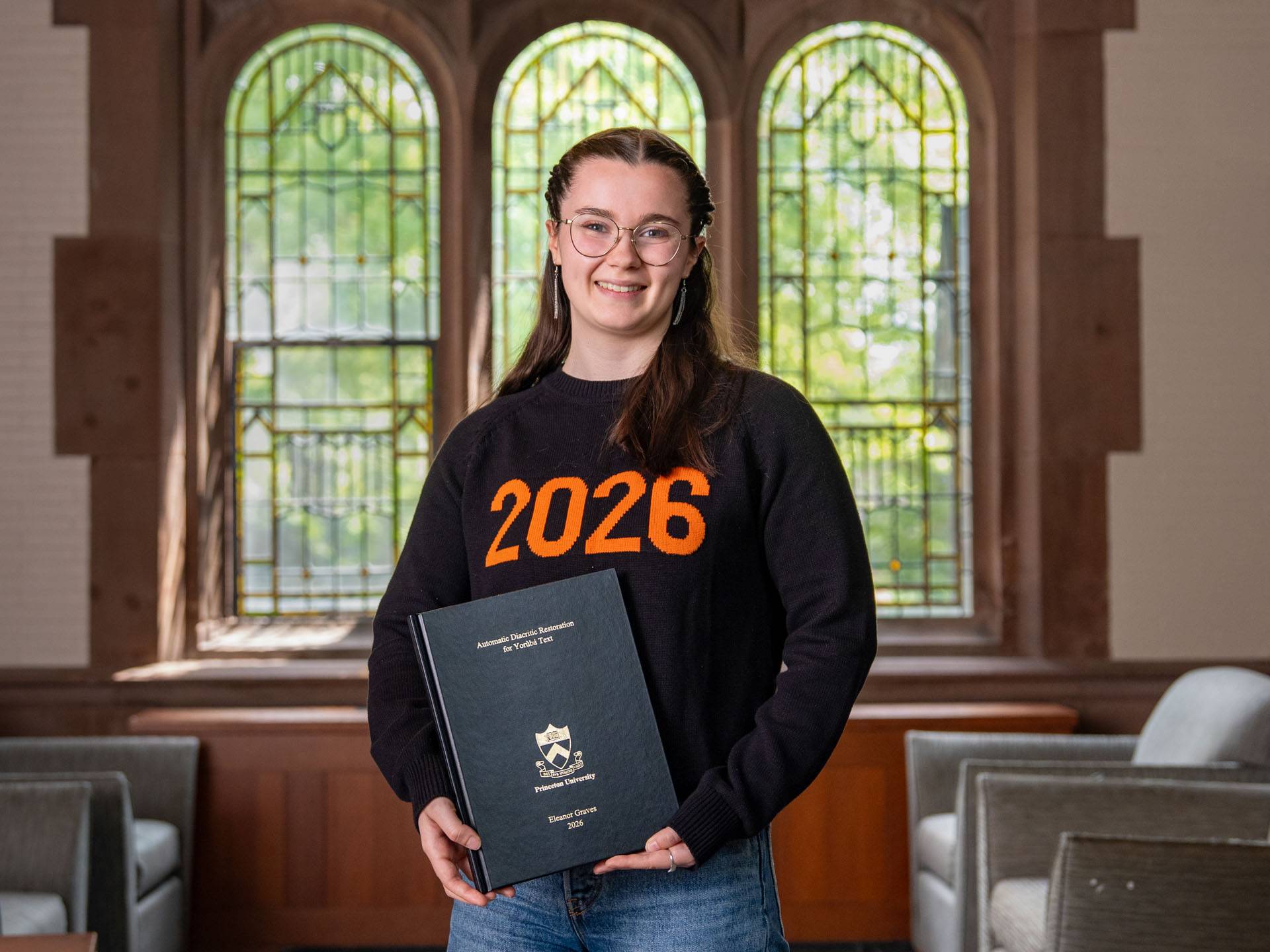 Nora Graves stands proudly holding her thesis and wearing a "Class of 2026" sweatshirt
